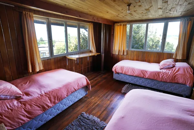 Un ambiente acogedor con camas de sábanas rosas y ventanales que permiten la entrada de luz natural, ideal para disfrutar de la vista al exterior. - Conguillío - Hostal Micelio Villarrica