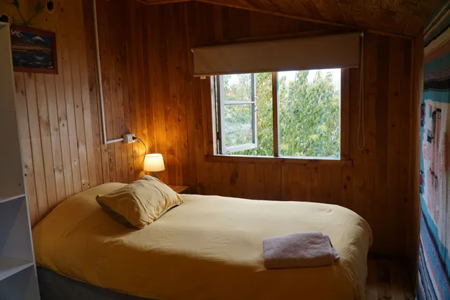 Decoración rústica que incluye una lámpara cálida y cortinas claras. Ventana abierta que deja entrar frescura del exterior. - Torres del Paine - Hostal Micelio Villarrica