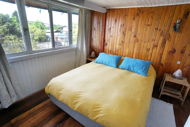 Habitación luminosa con una cama matrimonial de tonos cálidos, almohadas azules y detalles simples que crean un ambiente tranquilo y confortable — Rapa Nui — Hostal Micelio, Villarrica.