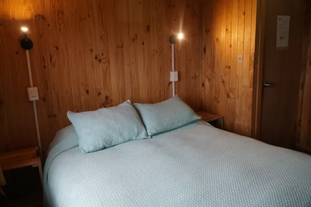 Espacio acogedor que destaca por su cama con almohadas suaves y lámpara cálida - Queulat - Hostal Micelio Villarrica