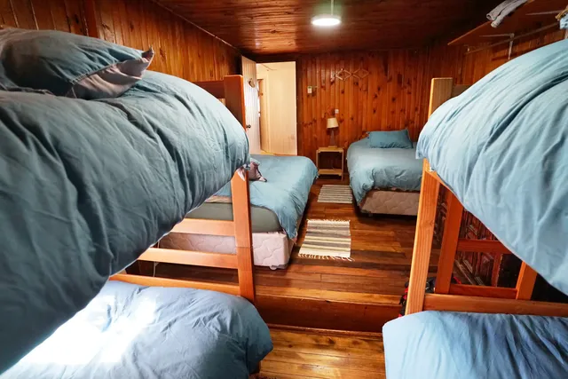 Habitación amplia con literas y camas individuales, revestida en madera y con luz natural que resalta su ambiente cómodo y funcional, ideal para grupos o familias — Laguna San Rafael — Hostal Micelio, Villarrica.