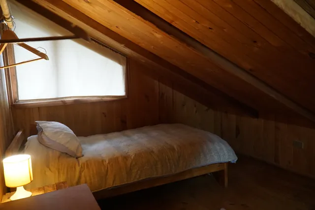 Espacio acogedor con cabecera de madera, manta tejida y luz cálida, ideal para disfrutar de vistas al volcán desde el piso alto. - Huerquehue - Hostal Micelio Villarrica
