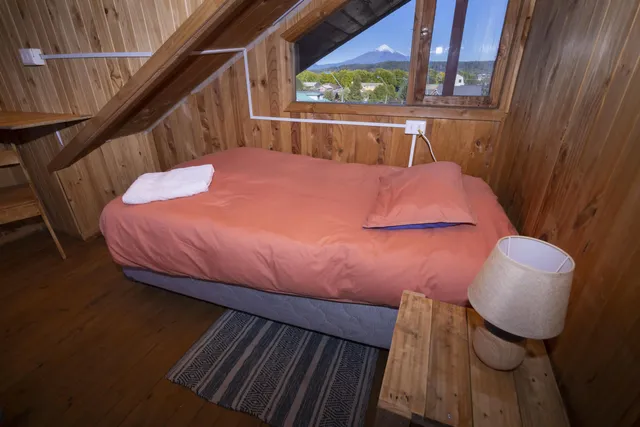 Estancia en piso alto con decoración de madera, alfombra tejida y luz natural, ideal para disfrutar del paisaje volcánico. - Pumalin - Hostal Micelio Villarrica