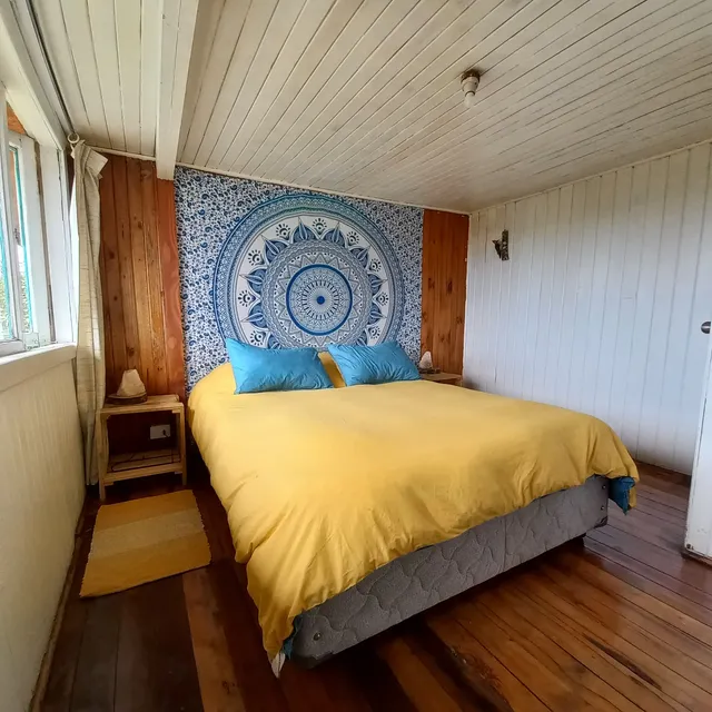 Habitación luminosa con cama matrimonial, tapiz de mandala azul y piso de madera, un espacio cálido y tranquilo — Rapa Nui — Hostal Micelio, Villarrica.
