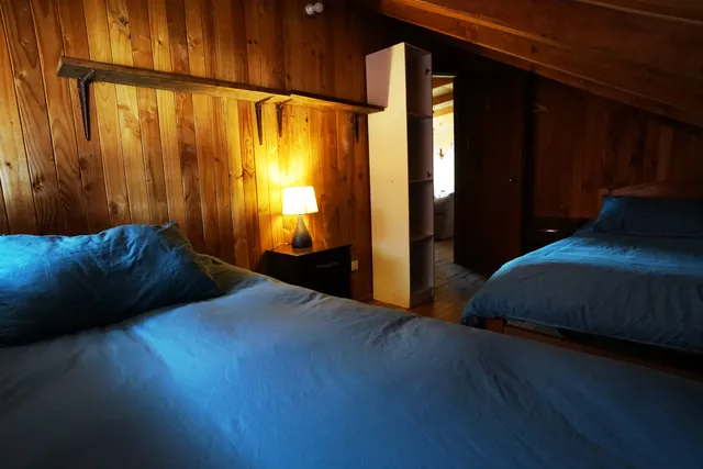 Habitación con revestimiento de madera, camas confortables y una luz cálida que realza su ambiente tranquilo y acogedor — Nahuelbuta — Hostal Micelio, Villarrica.