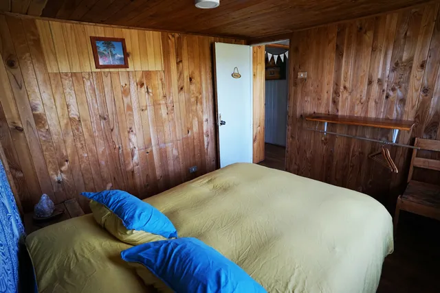Habitación con cama matrimonial, detalles simples y una cálida iluminación natural que realza los tonos de madera, ofreciendo un ambiente tranquilo y ordenado — Villarrica — Hostal Micelio, Villarrica.
