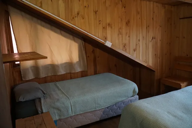 Destacan las camas con mantas tejidas y una mesa de madera, iluminadas por luz natural, creando una atmósfera tranquila con vista al volcán. - Queulat - Hostal Micelio Villarrica