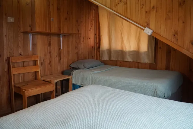 Habitación con cama matrimonial y una individual, ambiente cálido con detalles naturales y una atmósfera tranquila, ideal para familias — Queulat — Hostal Micelio, Villarrica.